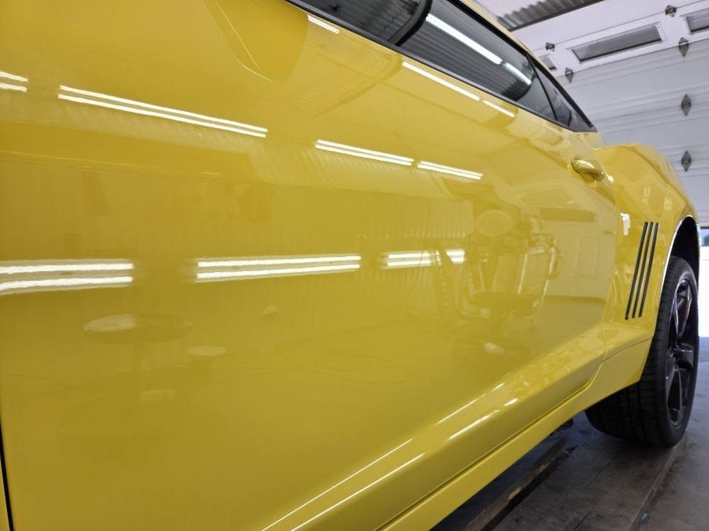 Panneau de carrosserie jaune poli reflétant les lampes du plafond de l'atelier — brillance miroir